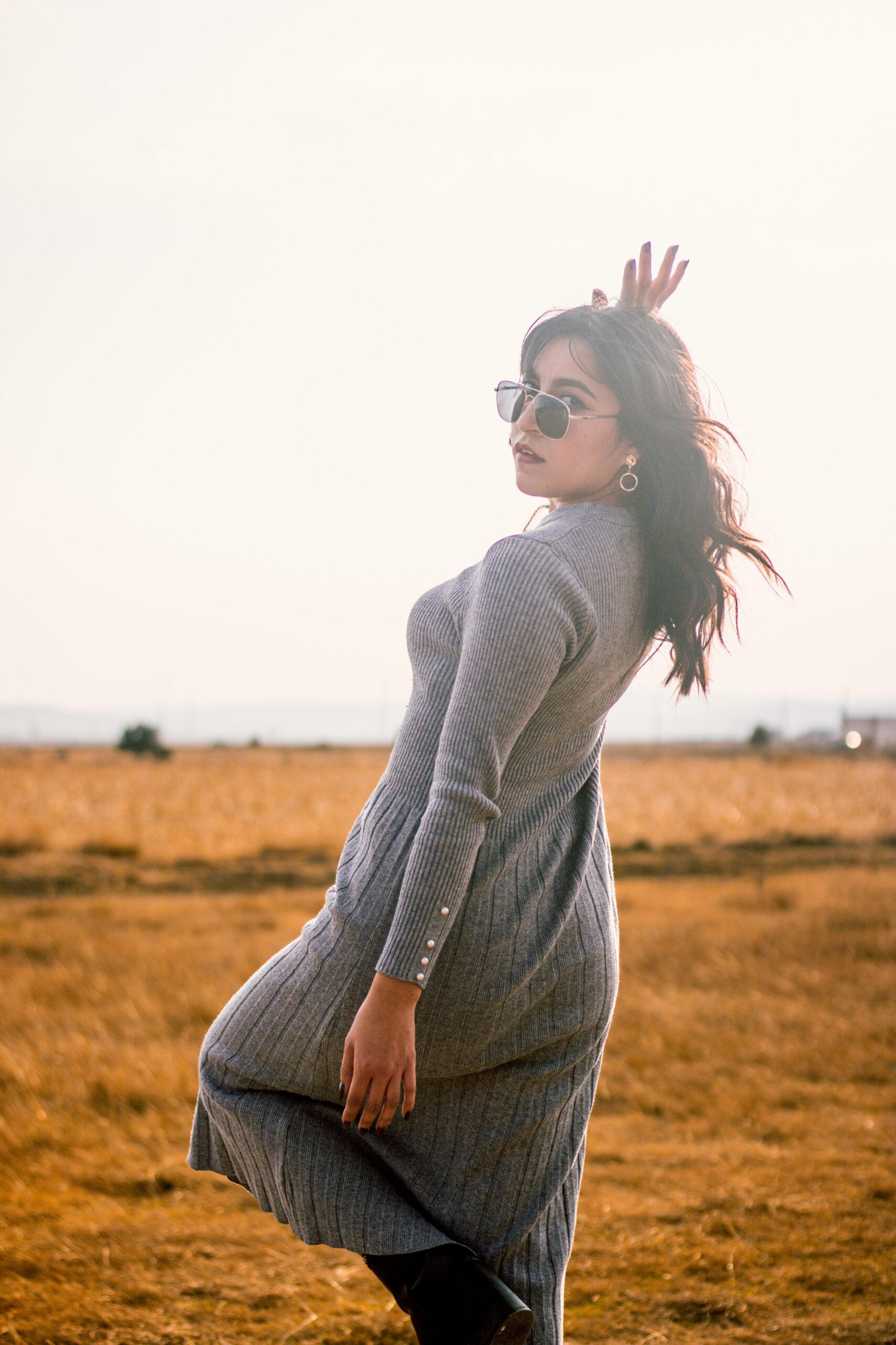 Woman wearing a grey ribbed midi dress posing in an open field.