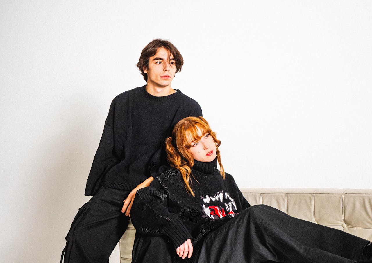 My Post A fashionable couple dressed in black sits and poses thoughtfully on a couch.