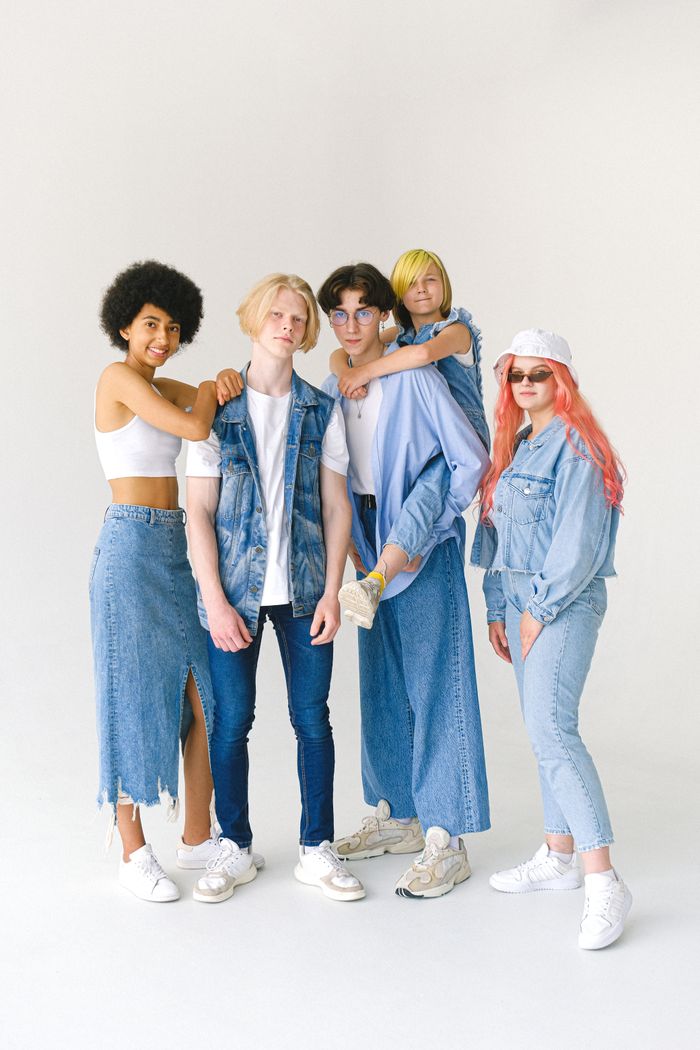 About Full body group of smiling teenage friends in jeans clothes standing against white background and looking at camera