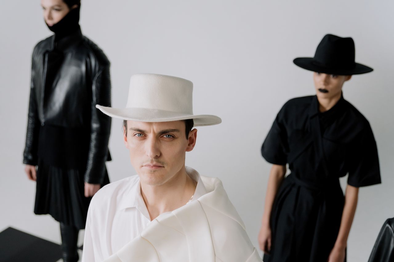 Stylish individuals in monochrome fashion with distinctive hats posing indoors.